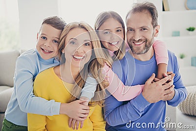 Portrait of idyllic family mom dad hug piggyback two little preteen kids boy girl in house indoors Stock Photo