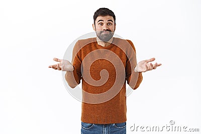 Portrait of indecisive, clueless attractive bearded man in brown sweatshirt, dont know, spread hands sideways and smirk Stock Photo