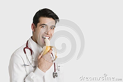 Portrait of Indian male doctor eating banana over white background Stock Photo