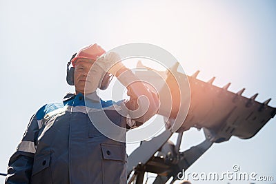Portrait industrial worker driver in helmet and headphones against background of excavator. People mining concept Stock Photo