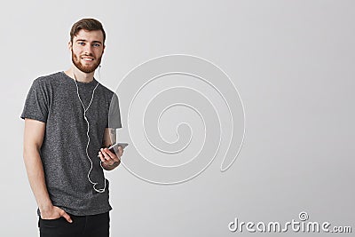 Portrait of joyful attractive european man with beard and tattoo on arm, listening to favourite music in earphones Stock Photo