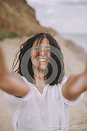 Portrait of joyful boho girl in white shirt having fun on sunny beach. Carefree stylish woman smiling and relaxing on seashore. Stock Photo