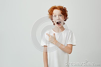 Portrait of joyful ginger child with freckles posing with opened mouth and crazy expression, pointing at free space for Stock Photo