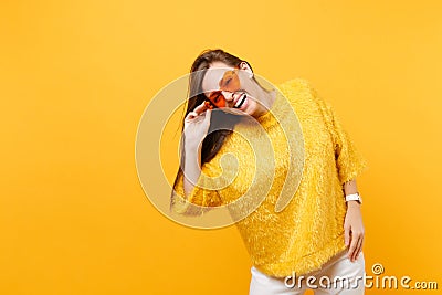 Portrait of joyful happy young woman in fur sweater, white pants holding heart orange glasses stand isolated on bright Stock Photo