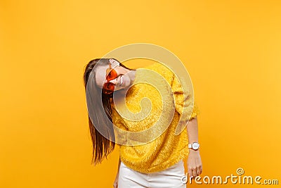 Portrait of joyful smiling funny young woman in fur sweater, white pants and heart orange eyeglasses isolated on bright Stock Photo
