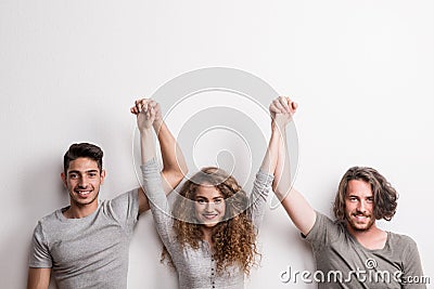 Portrait of joyful young girl with two boy friends standing in a studio, lifting hands. Stock Photo