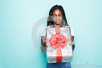 Portrait of joyous african woman with afro hairdo holding gift box and smiling in happiness over blue background Stock Photo