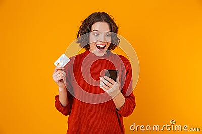 Portrait of joyous woman using cell phone and credit card while standing isolated over yellow background Stock Photo