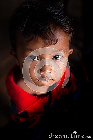 Portrait of a Khmer little boy with spot light pointing on him, cute black eyes looking up at camera Editorial Stock Photo