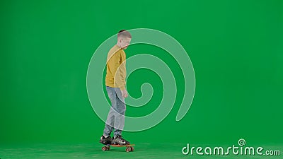 Portrait of kid boy on chroma key green screen. Schoolboy in jeans standing riding on skateboard through the scene Stock Photo