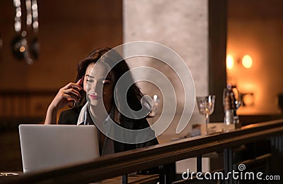 Portrait of laughing and beautiful businesswoman speaking on the phone and working on her laptop in modern restaurant Stock Photo