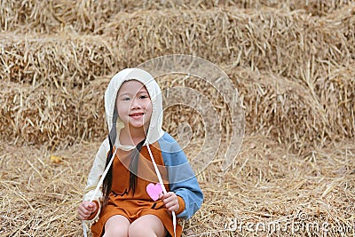 Portrait of little Asian child girl put on hood on head sitting on pile of straw Stock Photo