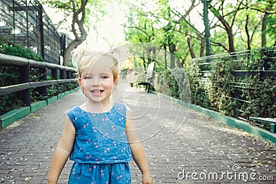 Portrait of little blondy toddler Girl Smiling at Camera. Happy kid walking outdoors in the park or zoo. Family recreation, leasur Stock Photo