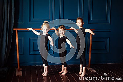 Portrait of 3 little children two girls ballerina and small boy dancer in black leotard practicing at ballet barre at dance studio Stock Photo