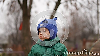 Portrait of little cute boy in a green jacket and hat with horns in the park Stock Photo