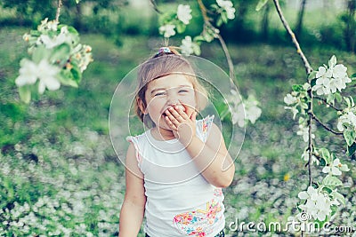 Portrait of little cute disheveled girl laughing and having fun outdoors among flowering trees in a sunny summer day Stock Photo