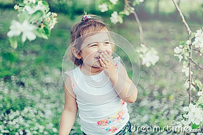 Portrait of little cute disheveled girl laughing and having fun outdoors among flowering trees in a sunny summer day Stock Photo