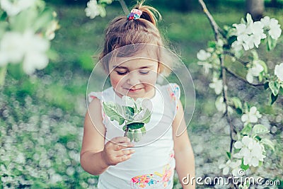 Portrait of little cute disheveled girl laughing and having fun outdoors among flowering trees in a sunny summer day Stock Photo