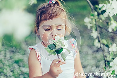 Portrait of little cute disheveled girl laughing and having fun outdoors among flowering trees in a sunny summer day Stock Photo