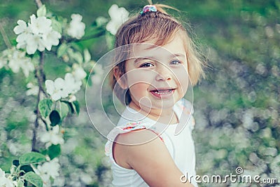 Portrait of little cute disheveled girl laughing and having fun outdoors among flowering trees in a sunny summer day Stock Photo