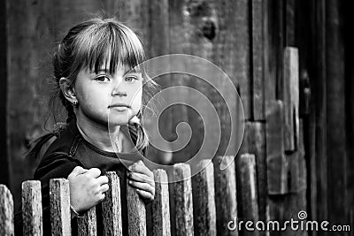 Portrait of little cute girl near vintage rural fence. Black and white photography. Stock Photo