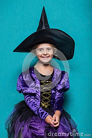 Portrait of little girl in black hat and witch clothing. Halloween. Fairy. Tale. Studio portrait on blue background Stock Photo