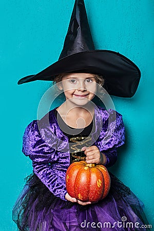 Portrait of little girl in black hat and witch clothing with pumpkin. Halloween. Fairy. Tale. Studio portrait on blue background Stock Photo