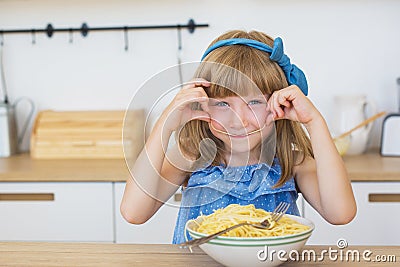 Portrait of a little girl funny eats a spaghetti from a dish and smiling Stock Photo