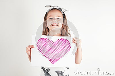 Portrait of little girl with long hair holding in hands sheet of paper with pink heart for present on white background. Stock Photo