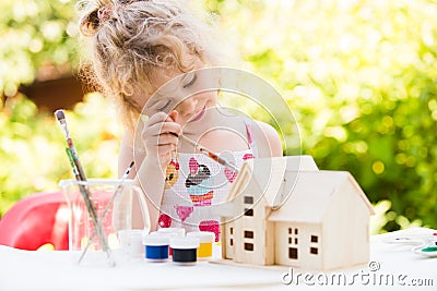 Portrait of little girl paints wooden model of house Stock Photo