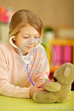 Portrait of little girl playing nurse, inspecting teddy bear with stethoscope Stock Photo