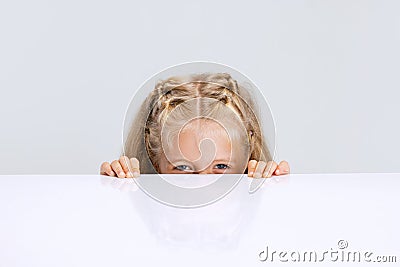 Portrait of little preschool girl, child playing hide-and-seek game isolated over white studio background. Stock Photo