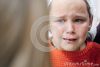 Portrait of little tearful girl in medical disposable cap crying in pain after ear piercing or other medical procedures Stock Photo