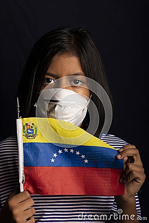 Portrait of little girl wearing medical mask and holding hopefully the flag of Venezuela Stock Photo