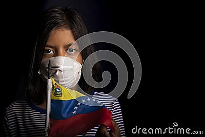 Portrait of little girl wearing medical mask and holding hopefully the flag of Venezuela Stock Photo