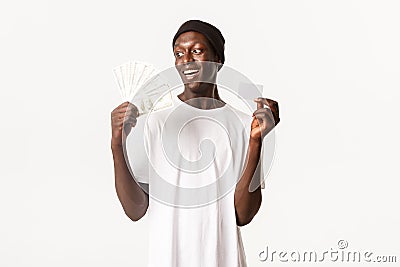 Portrait of lucky, excited african-american young guy looking happy at money, holding credit card, white background Stock Photo