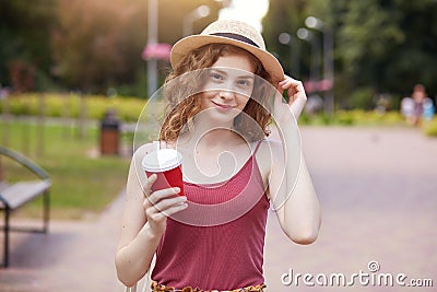 Portrait of magnetic positive female smiling sincerely, holding papercup of takeaway drink, having coffee break, touching her Stock Photo