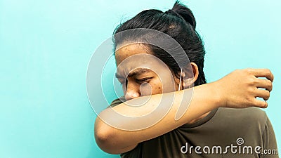 A portrait of a Malay man coughing and sneezing to his elbow neck with closing both eyes on isolated blue background Stock Photo