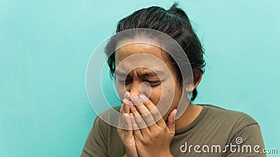 A portrait of a Malay man covering his mouth during coughing and sneezing with isolated blue background Stock Photo