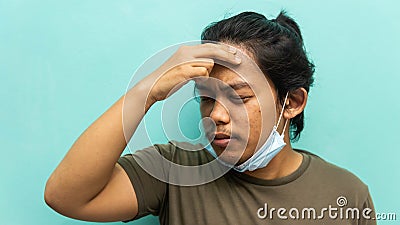 A portrait of a Malay man holding his head, having a headache with painful face reaction on isolated blue background Stock Photo