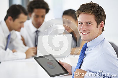 Portrait Of Male Executive Using Tablet Computer With Office Meeting In Background Stock Photo