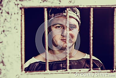 Portrait of male prisoner standing behind a prison grid in a jail cell Stock Photo