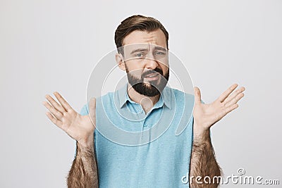 Portrait of a man with a beard raising his hands looking uncertain, standing near white wall. Husband tries to explain Stock Photo