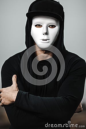 Portrait of man in black hoodie wearing white anonymous mask. Stock Photo