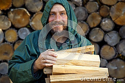 Portrait of a man with a bunch of chopped firewood. Bearded lumberjack with firewood for the fireplace. Stock Photo