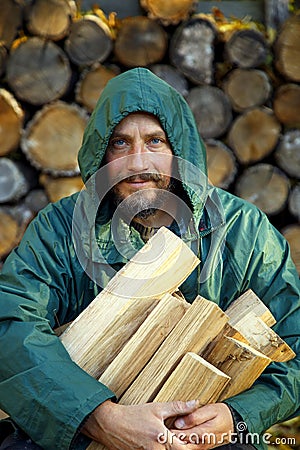 Portrait of a man with a bunch of chopped firewood. Bearded lumberjack with firewood for the fireplace. Stock Photo