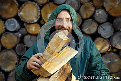 Portrait of a man with a bunch of chopped firewood. Bearded lumberjack with firewood for the fireplace. Stock Photo