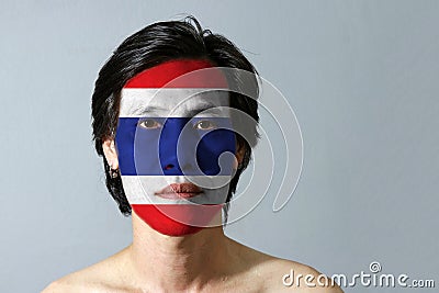 Portrait of a man with the flag of the Thailand painted on his face on black background. Stock Photo