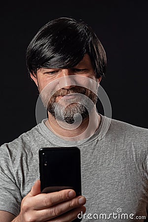 Portrait of a man with grey and black beard and long black hairs. Black background. Male dressed in grey t-shirt, smiling Stock Photo