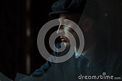 Portrait of a man in the image of an English retro gangster in Peaky blinders style through broken glass Stock Photo